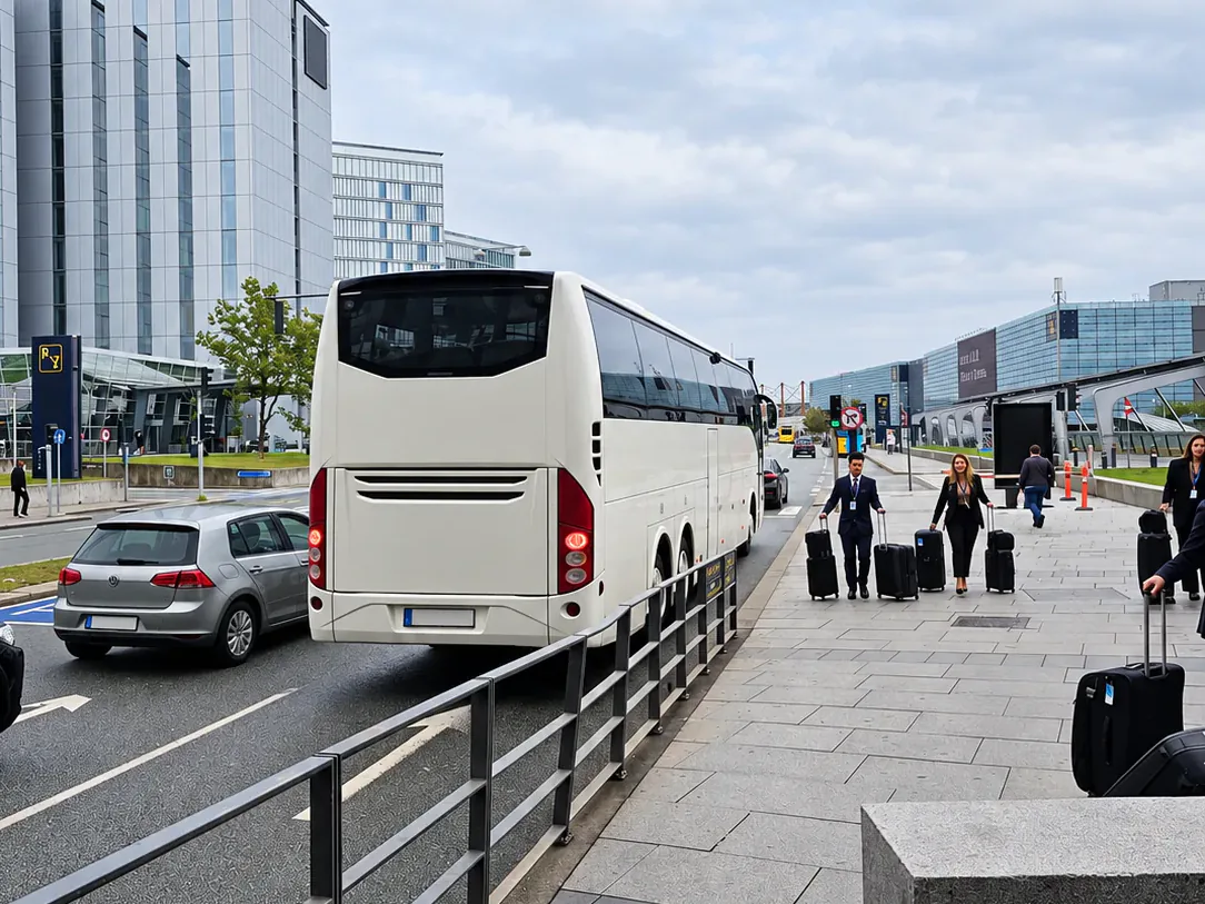 BusCom coach at the airport arrivals kerb, travellers with suitcases walking towards it
